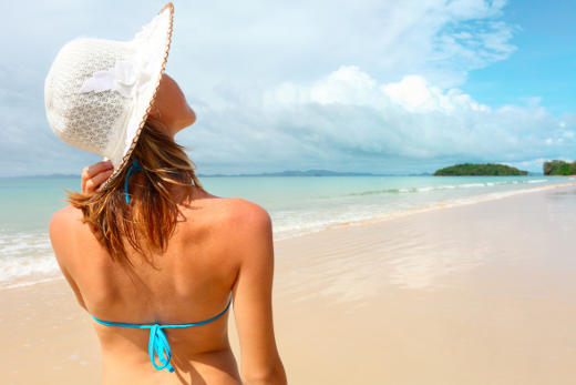 Young woman holding a straw hat and looking to a blue sky
