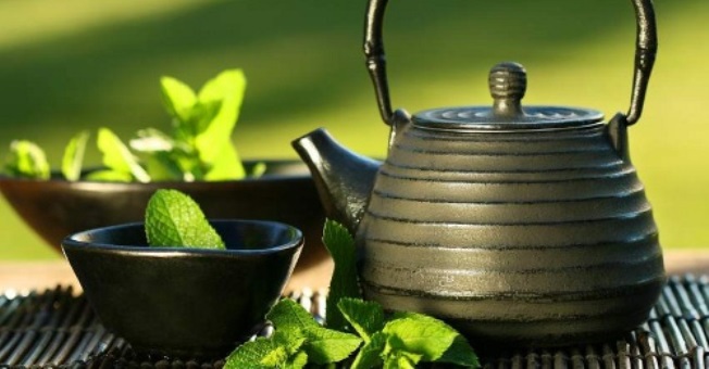 Black iron asian teapot with sprigs of mint for tea